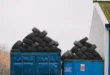 Piles of used tires on blue containers in an industrial recycling yard.
