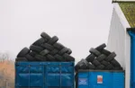 Piles of used tires on blue containers in an industrial recycling yard.