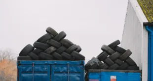 Piles of used tires on blue containers in an industrial recycling yard.