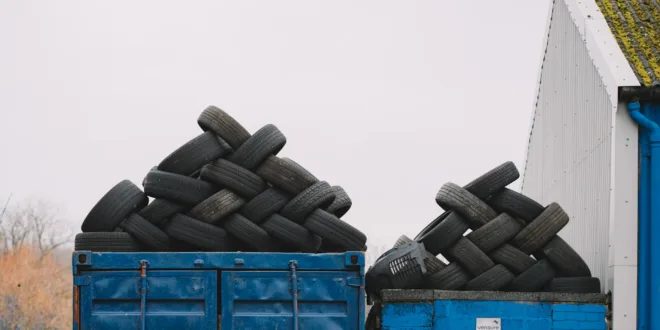 Piles of used tires on blue containers in an industrial recycling yard.