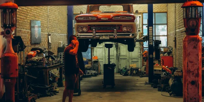 A red vintage truck is lifted in a Bangkok garage. Industrial setting with nostalgic automotive elements.