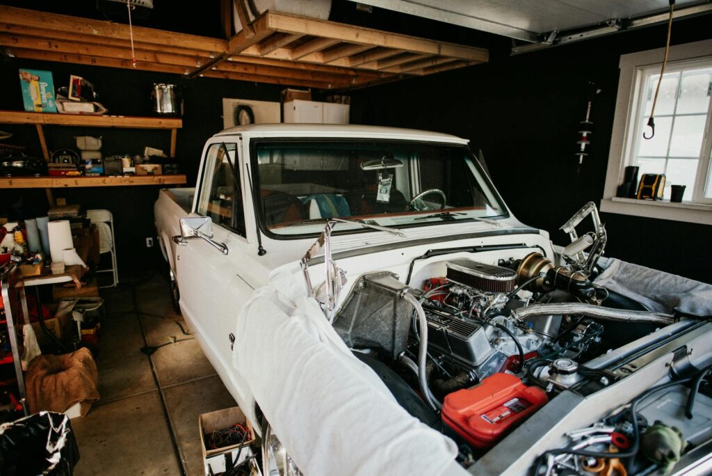 A vintage pickup truck undergoing engine repairs in a well-equipped home garage.