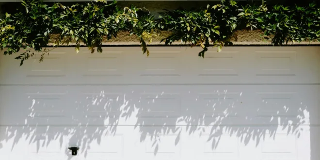 A closed white garage door adorned with lush green foliage casting shadows.
