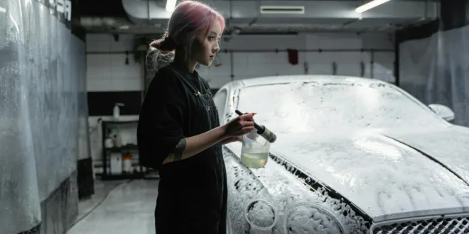 Asian woman washing luxury car in indoor car wash with foam.
