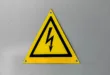 Close-up of a yellow high voltage warning sign mounted on a wall.