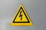 Close-up of a yellow high voltage warning sign mounted on a wall.