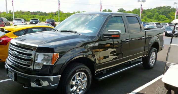 Black Ford F-150 pickup truck displayed at an outdoor dealership lot on a sunny day.