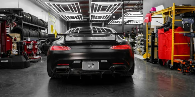 Rear view of a sleek black Mercedes Benz AMG GT in a modern, well-lit garage setting.