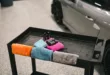 Colorful towels and detailing products on a cart beside a car in a garage.