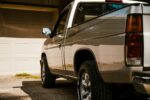 A silver pickup truck parked in a sunny residential driveway with closed garage doors.
