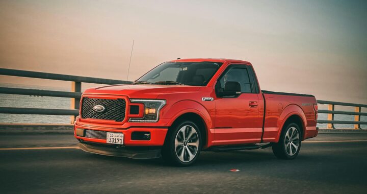 Red Ford F-150 truck driving on a bridge during sunset. Sleek and modern vehicle on the move.