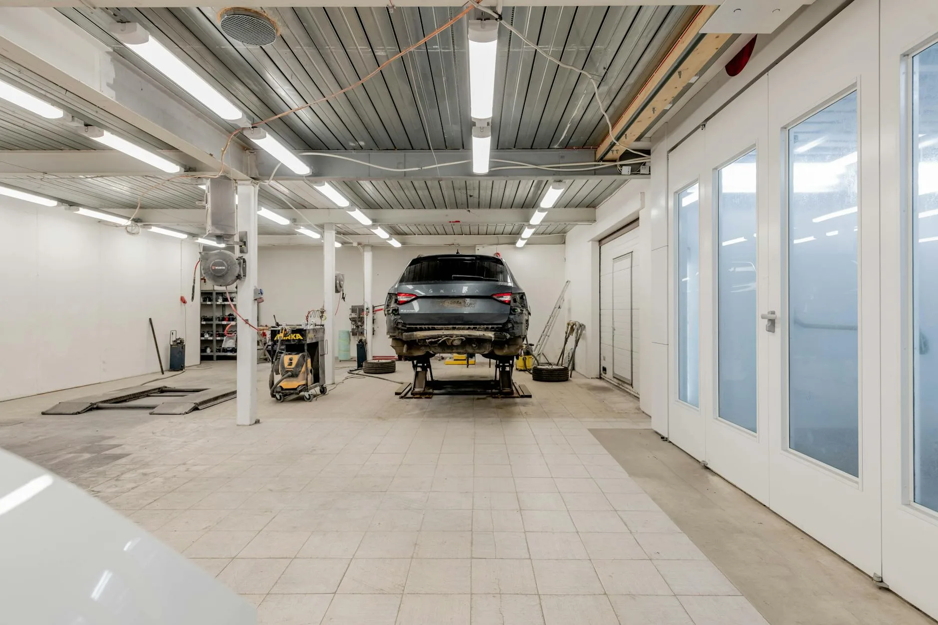 Well-lit garage with a car on a hydraulic lift ready for repair.
