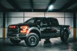 Bold black pickup truck with illuminated lights in an industrial garage.