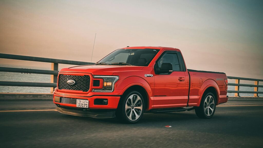 Red Ford F-150 truck driving on a bridge during sunset. Sleek and modern vehicle on the move.
