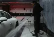 African American man cleaning a white car with a pressure hose in an indoor garage setting.
