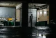 Dark industrial garage at night with open doors showing bins and equipment.