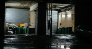 Dark industrial garage at night with open doors showing bins and equipment.