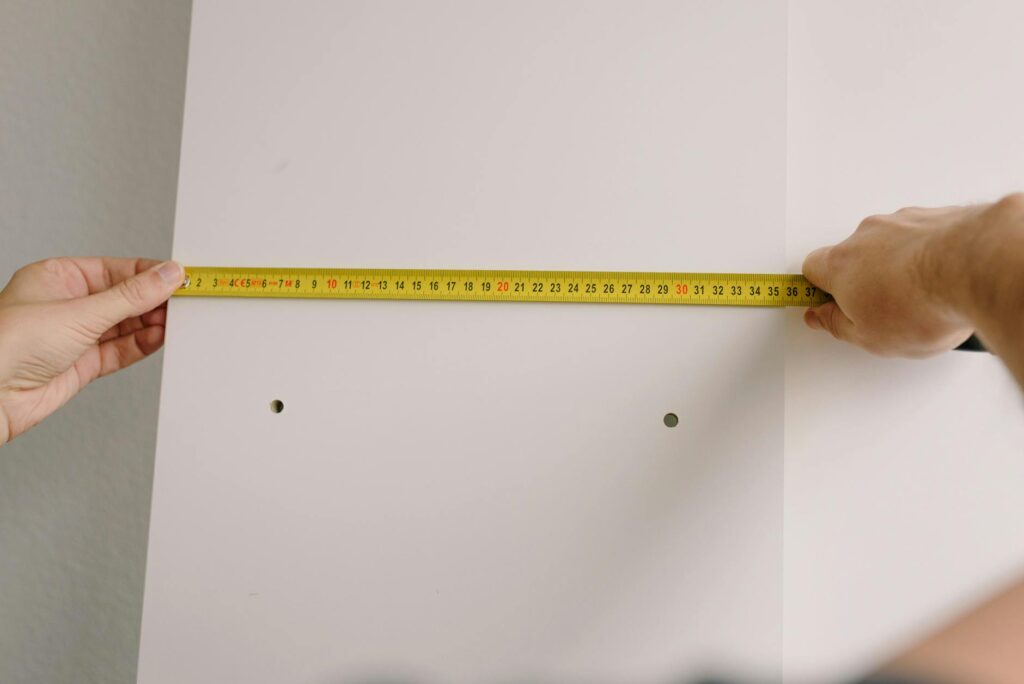 Crop unrecognizable male using measuring tape to make marks on white wooden board
