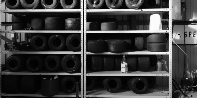Monochrome image of stacked go-kart tires on sturdy shelves, showcasing various wheel sizes.