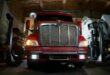 Front view of a red truck in a dimly lit automotive repair shop with a focus on the grill and headlights.