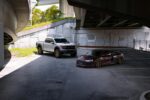 Silver truck and red sports car parked under a highway overpass in an urban setting.