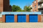 Three blue garage doors in a brick building on a sunny day.