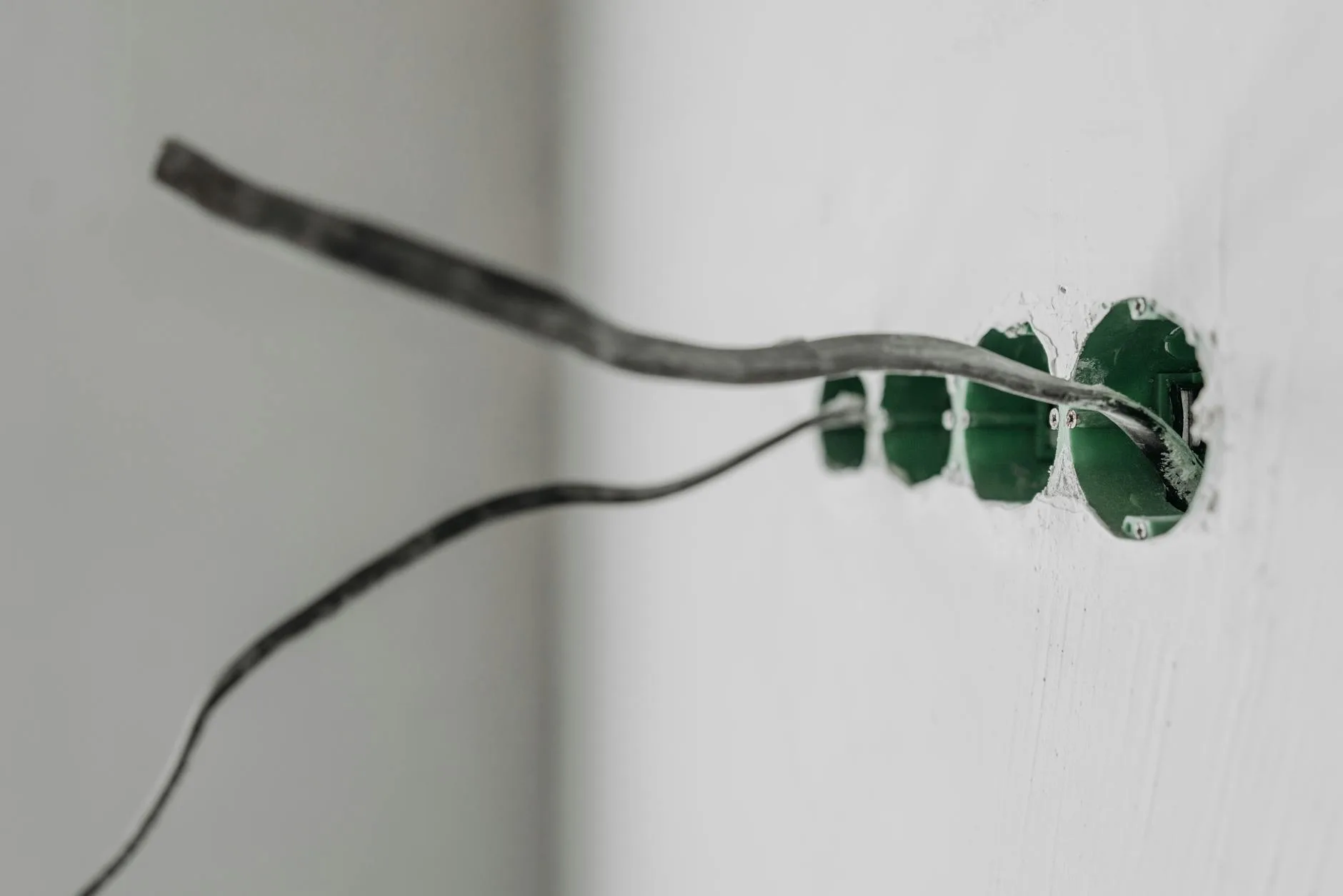 Unfinished electrical outlet installation with exposed wires on a white wall.