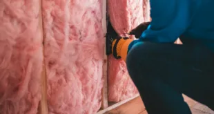 Crop unrecognizable worker in gloves sitting on haunches and insulating with pink stone wool