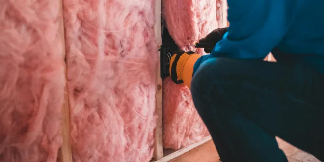 Crop unrecognizable worker in gloves sitting on haunches and insulating with pink stone wool