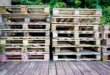 A pile of wooden pallets on a wooden deck surrounded by greenery, suitable for industry and recycling themes.