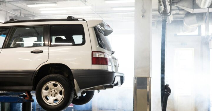 A white SUV is elevated on a lift inside an auto repair shop for maintenance.